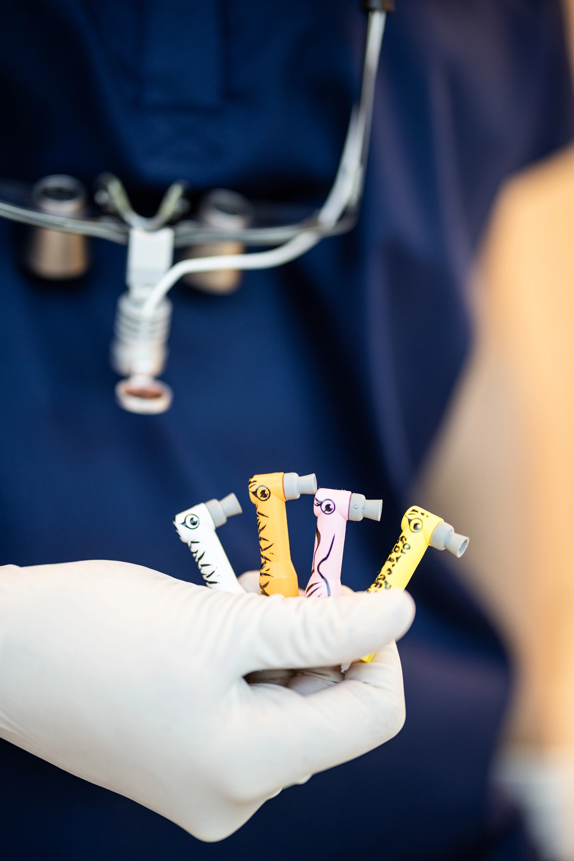 Bunte kindgerechte Zahnarzt-Handstücke in Tieroptik in einer behandschuhten Hand